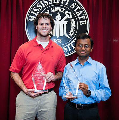 Students standing in front of MSU seal and holding trophies